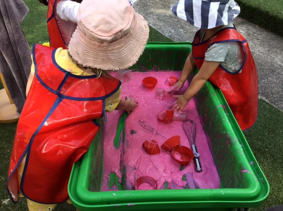 Children in smocks playing in a tub of pink water