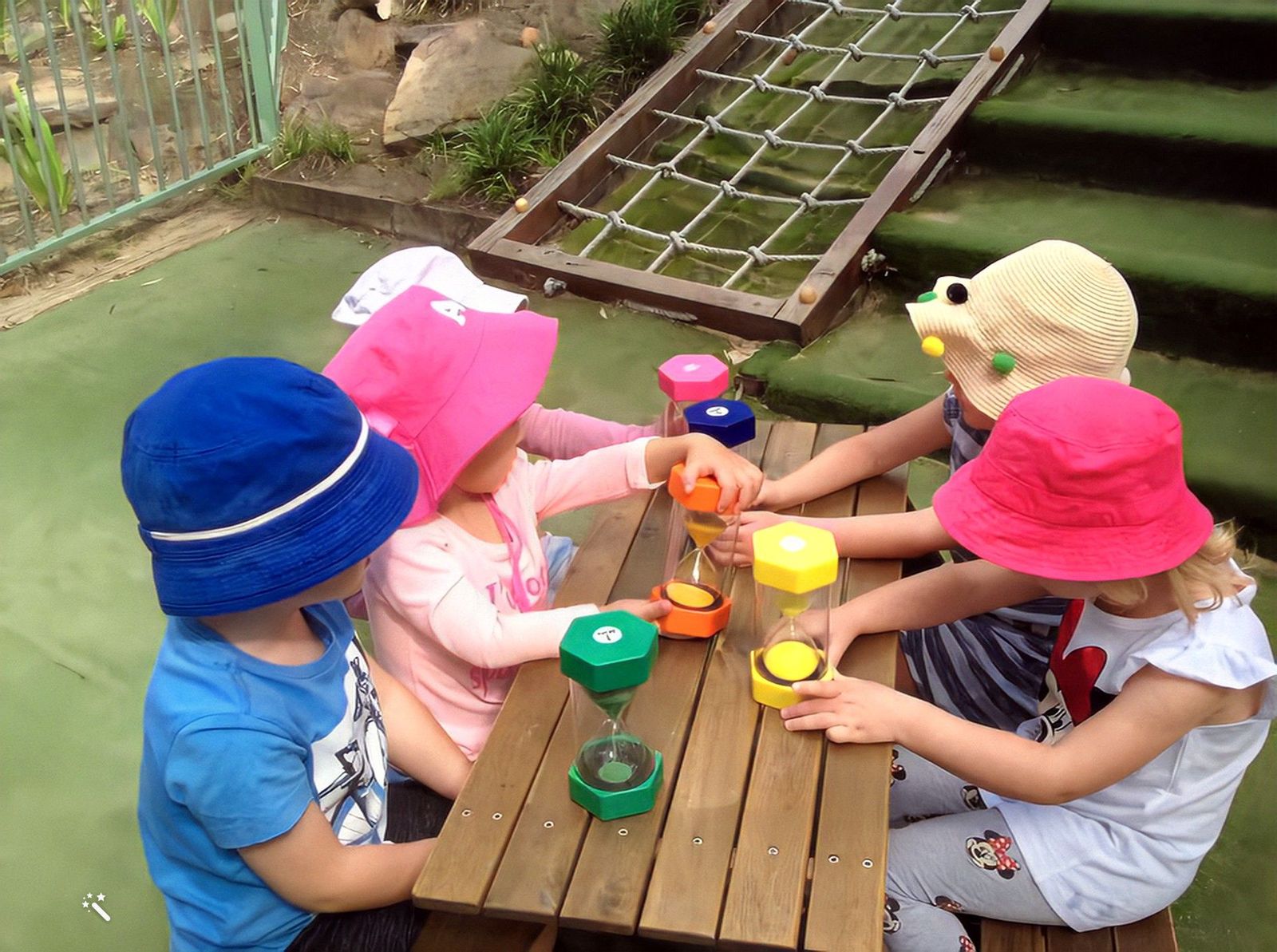 Children playing with coloured sand timers at an outdoor table